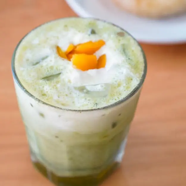 Matcha in a clear glass with yellow bits of mango on top