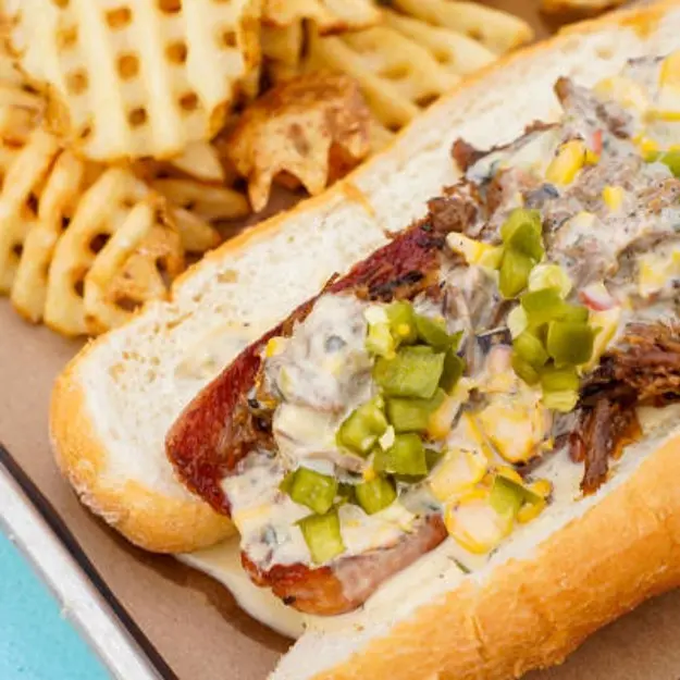 Hotdog with relish and toppings next to waffle fries on a silver plate